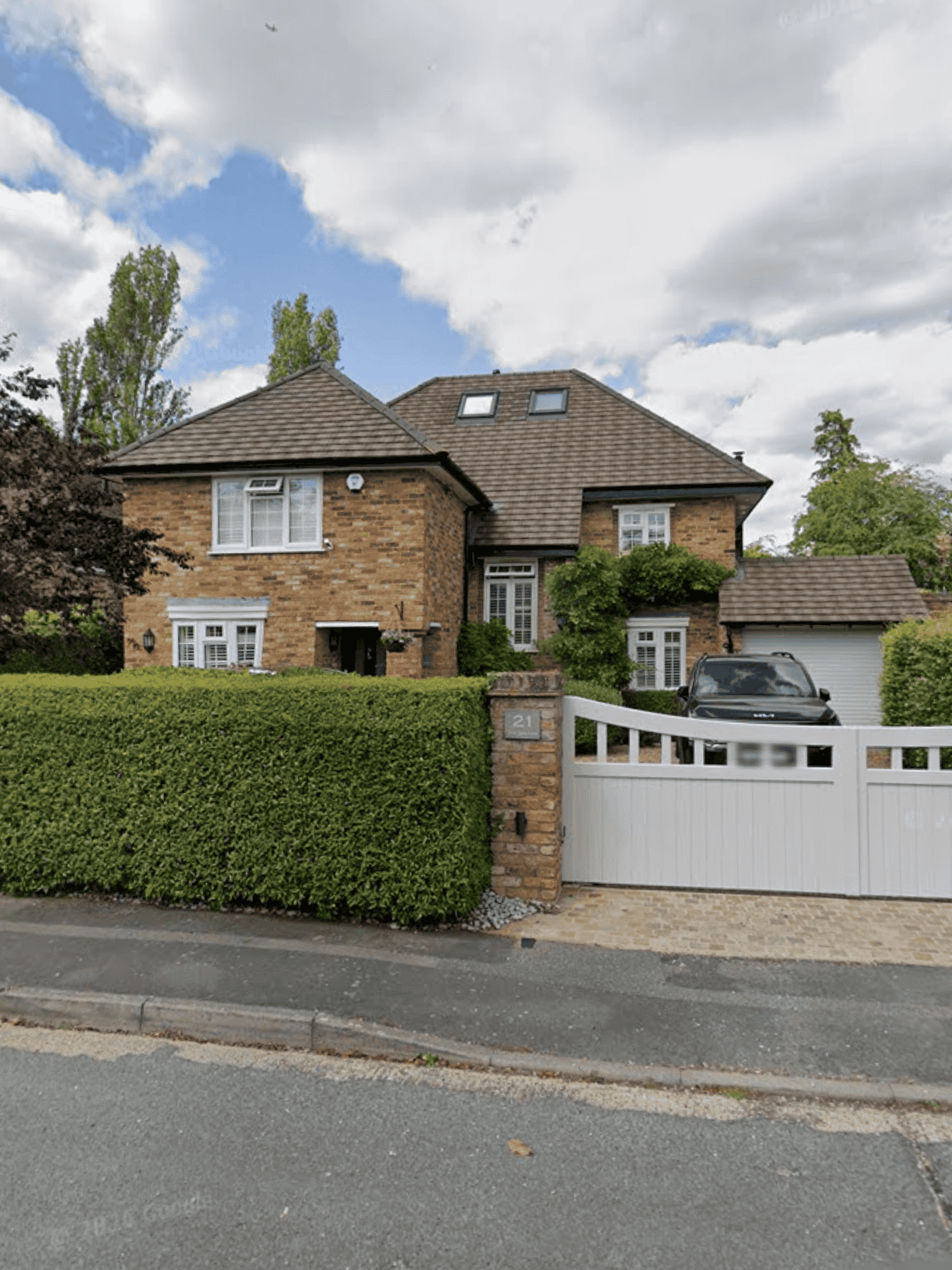 Large brick house with a driveway and white gate in a suburban neighbourhood.