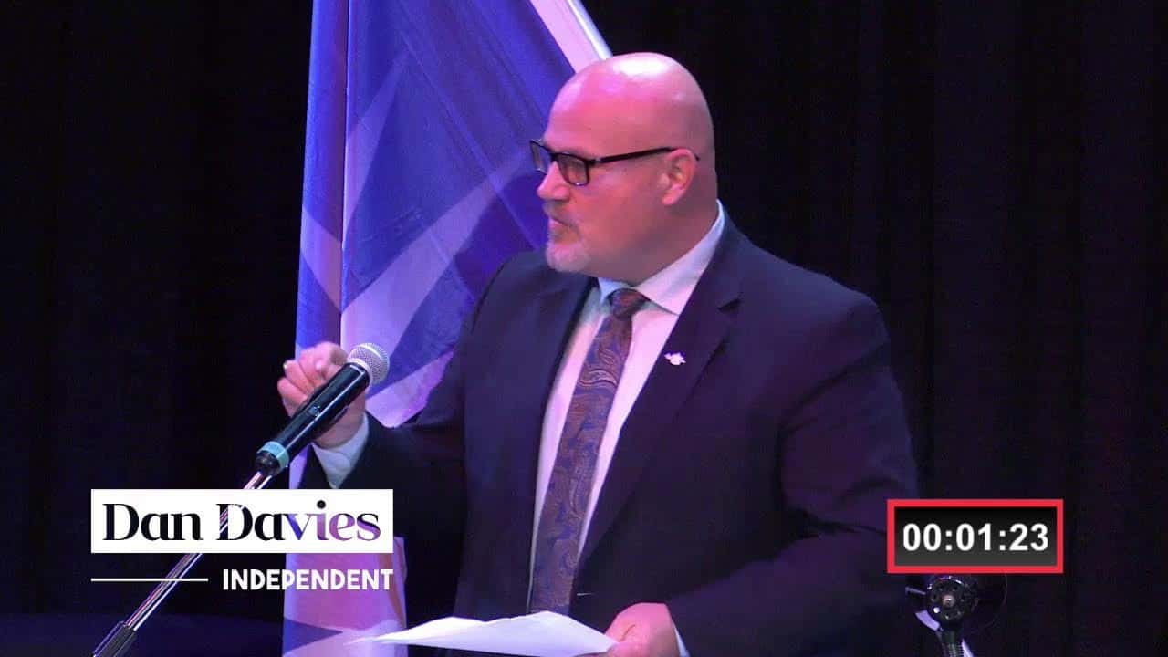 Bald man in suit speaking at a podium with Canadian flag in background for MooseMedia promotional content.