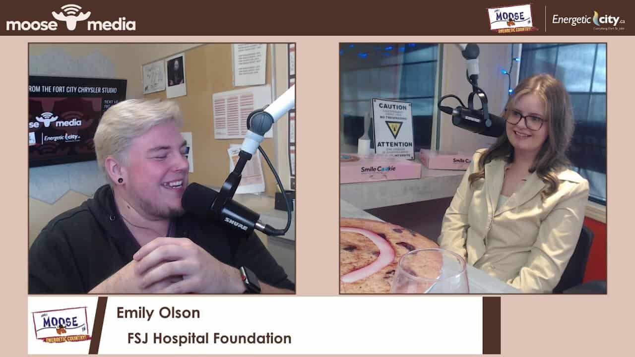 Brightly lit radio studio featuring two hosts engaged in conversation, with branded signage and professional microphones in use.