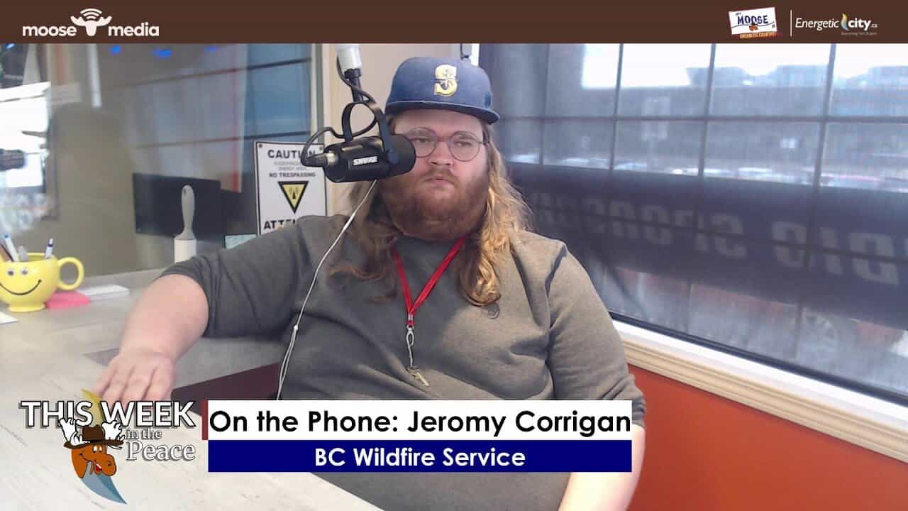 Radio host with microphone wearing baseball cap during BC wildfire service interview.