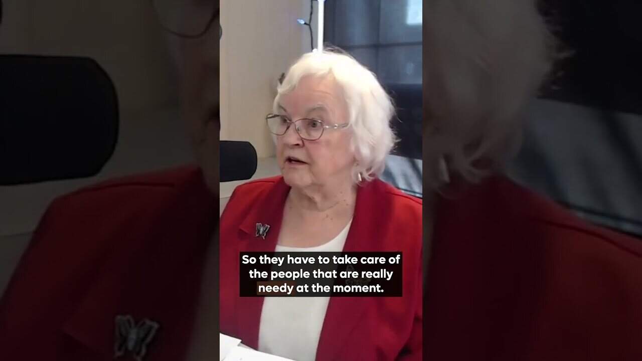 Elderly woman speaking into microphone about caregiving and needy individuals.