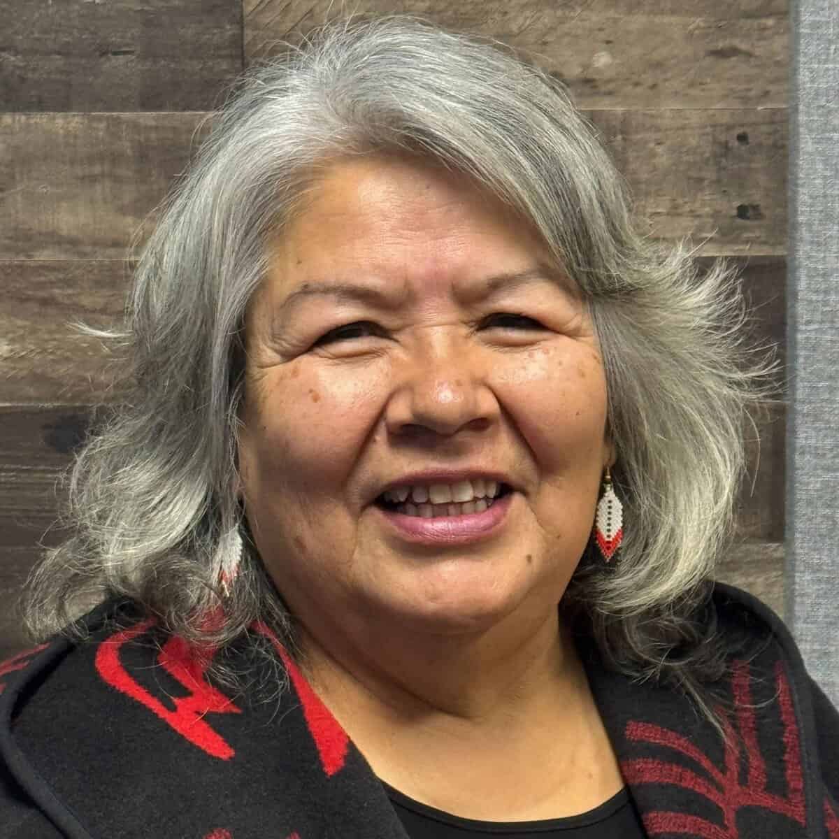 Close-up of smiling woman with gray hair and cultural earrings.
