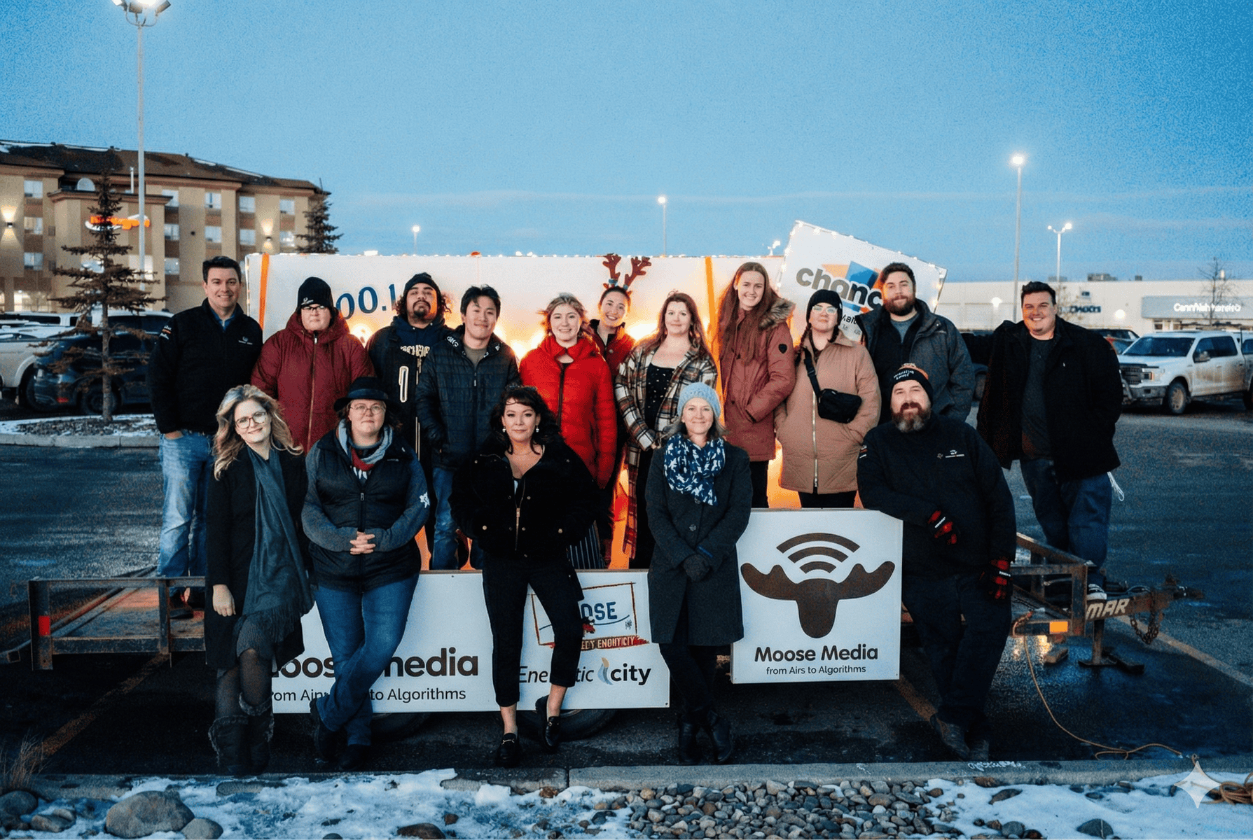 Group photo of MooseMedia staff and clients in a parking lot during winter evening.