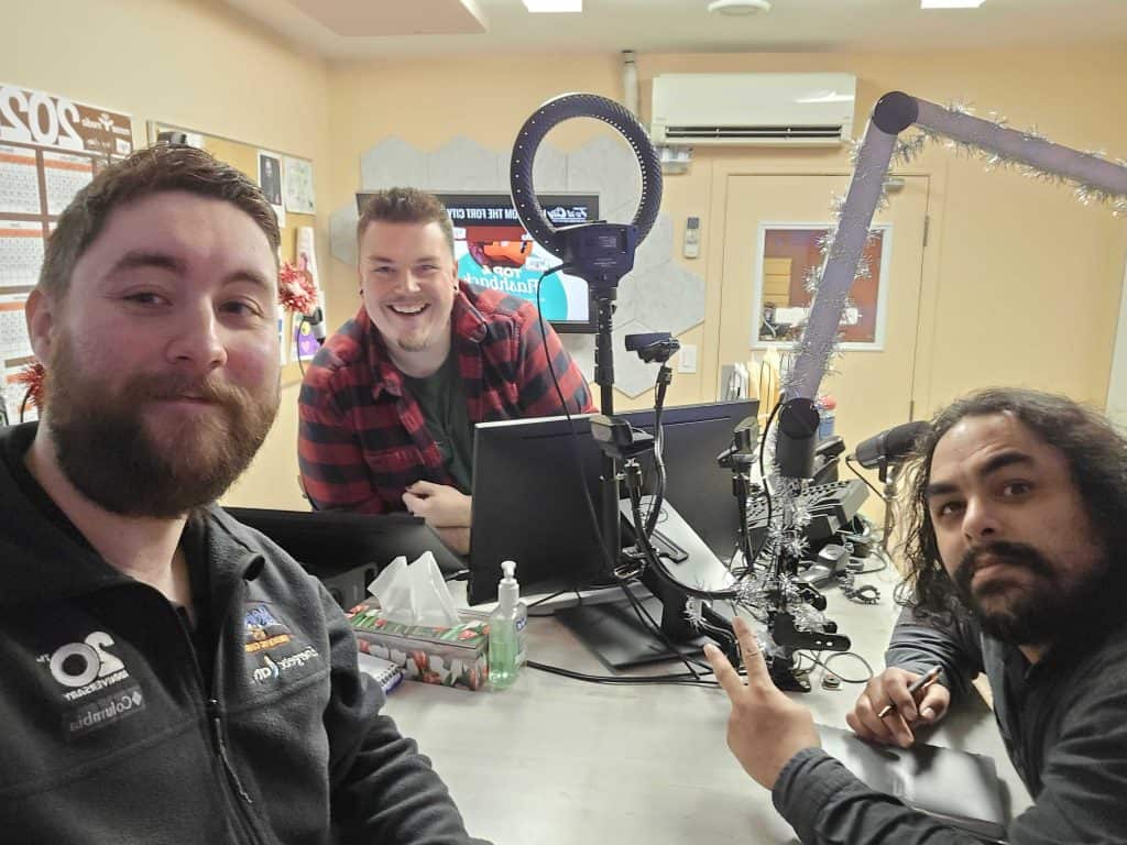 Group of men in studio with microphones, computers, and holiday decorations for content creation.