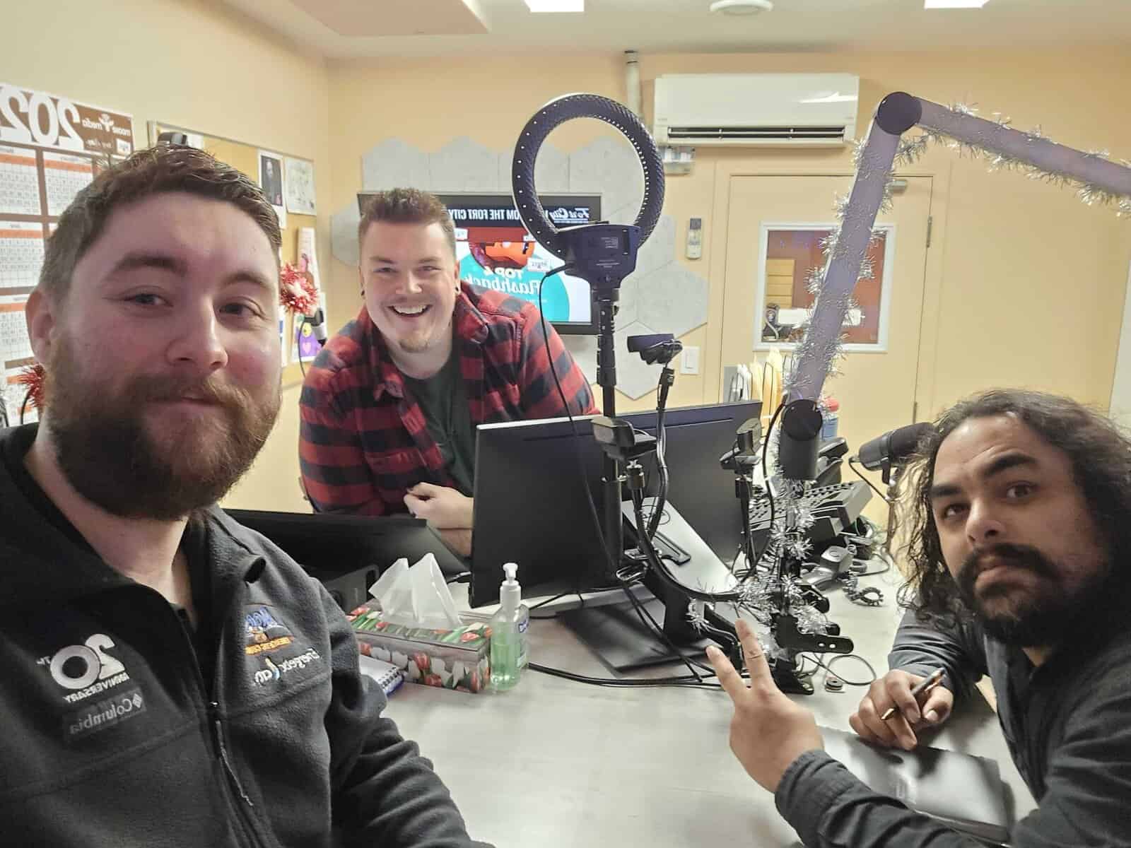Group of men in studio with microphones, computers, and holiday decorations for content creation.