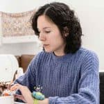 Woman sewing with a focused expression in a cozy room.