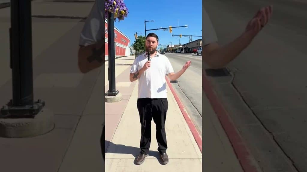 Man with microphone reporting news outdoors in a city setting.