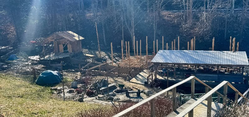 Mountain harbour construction site with timber and outdoor structures in a forest setting.