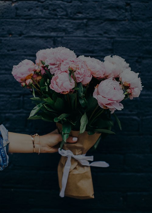 Pink peony bouquet in brown paper wrapping on dark wall background.