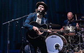 Stylish musician playing guitar and singing at Mountain Harbour live music event.