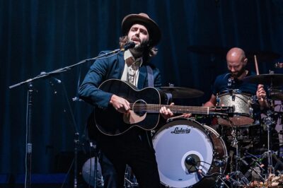 Stylish musician playing guitar and singing at Mountain Harbour live music event.