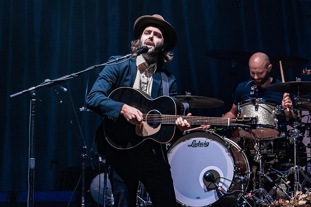 Stylish musician playing guitar and singing at Mountain Harbour live music event.
