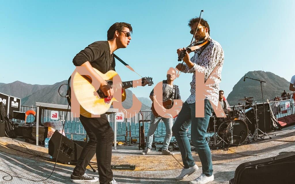 Mountain harbor outdoor music event with band playing on a stage by the lake in mountain scenery.