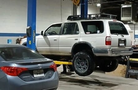 Service vehicle lifted on hydraulic lift at Murdock & Son Automotive.