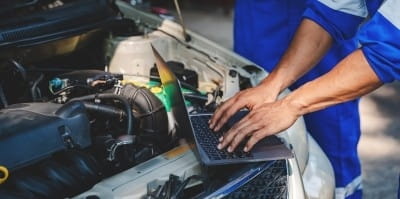 Technician using laptop for car diagnostics under the hood.