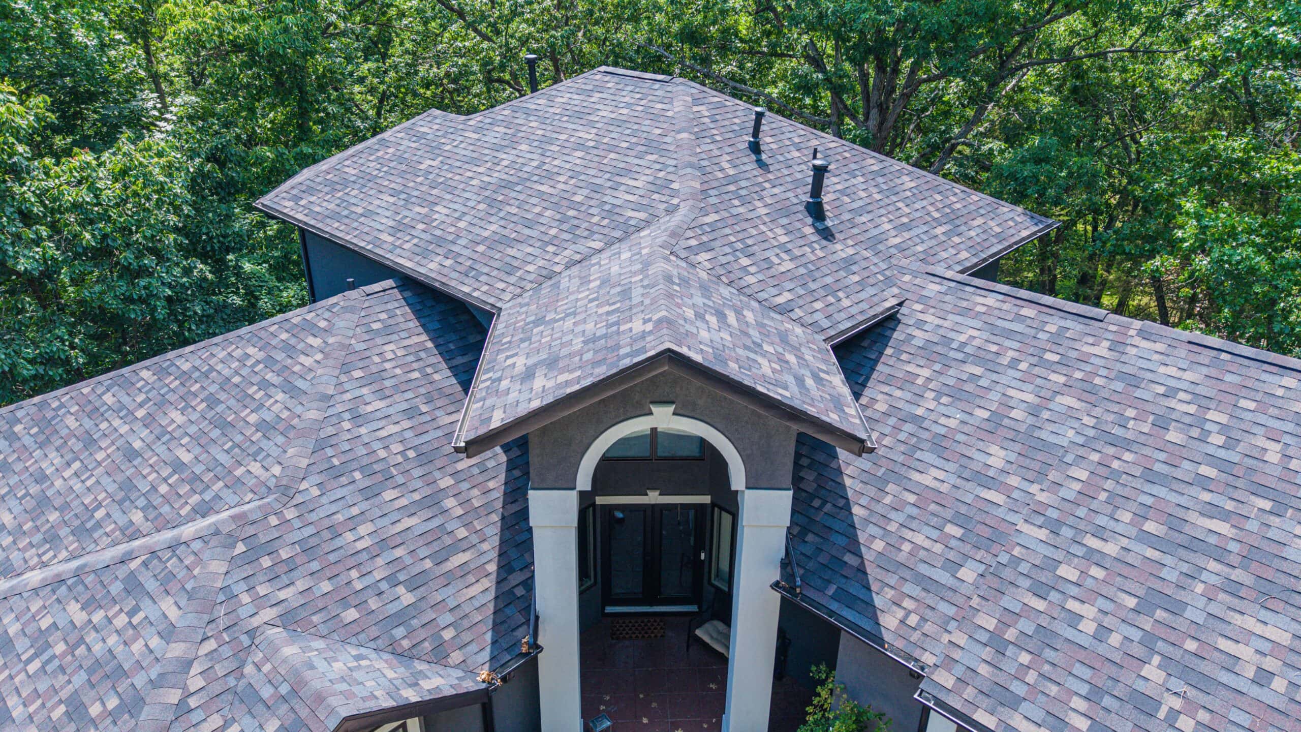 Roofing installation featuring high-quality shingles on a spacious home in a wooded area.