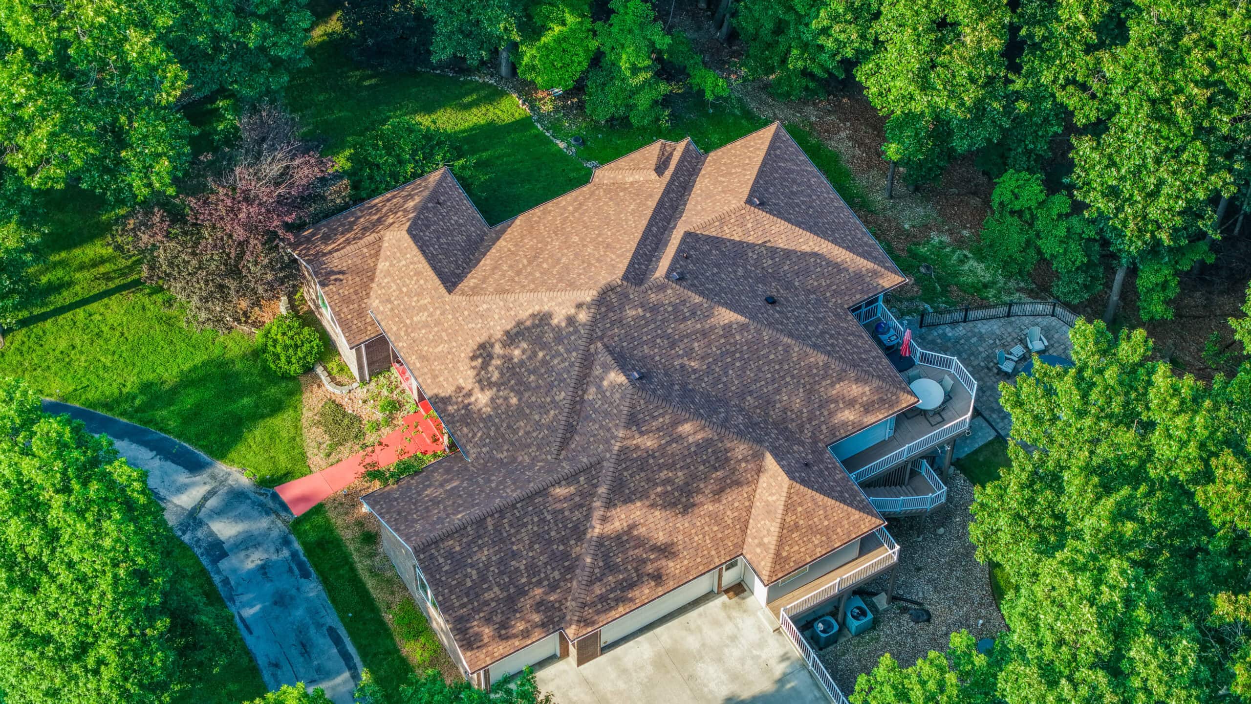 Aerial view of a house with a new brown shingle roof surrounded by trees.