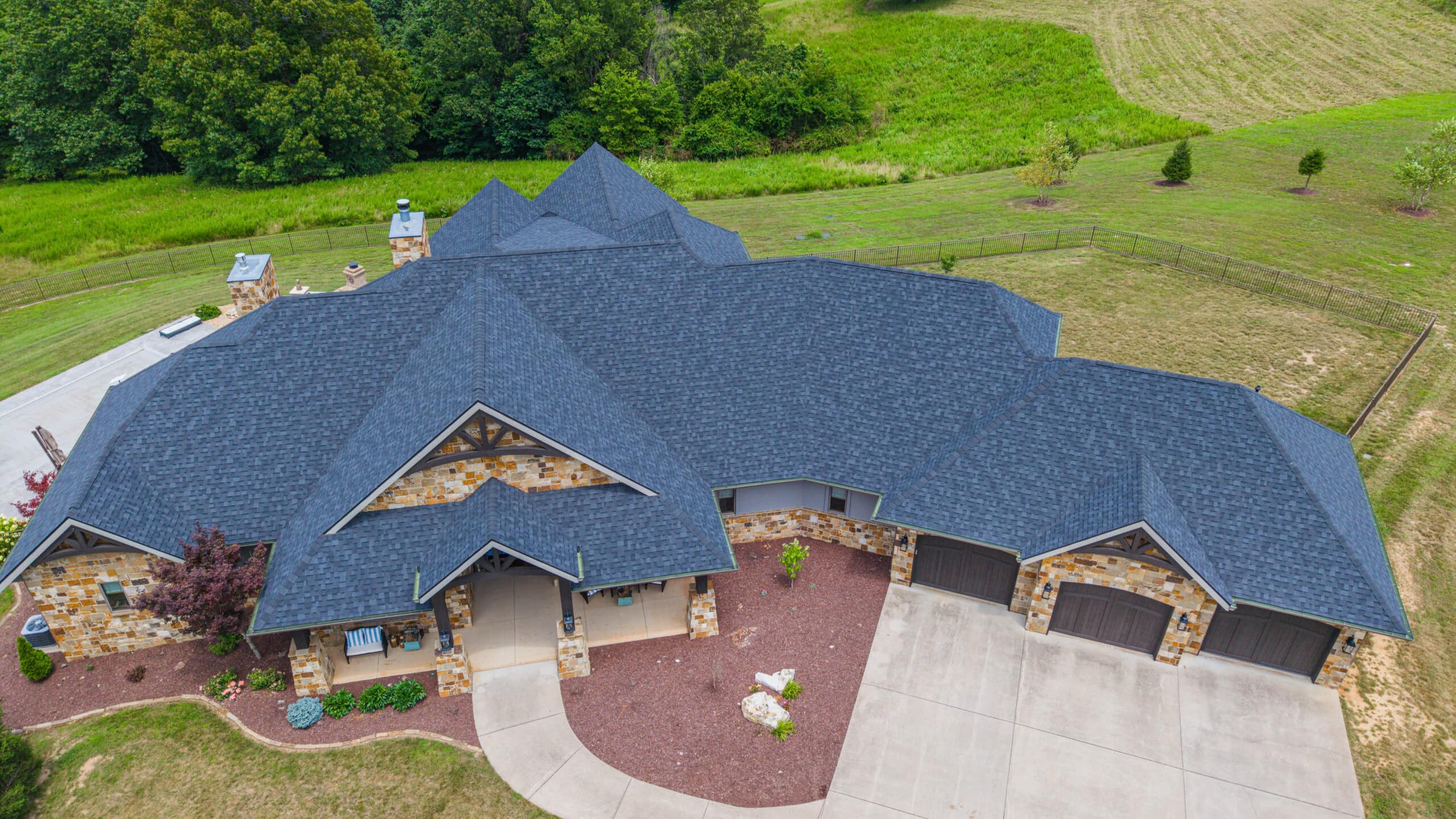 Aerial view of a large house with new asphalt shingle roofing in a lush green setting.