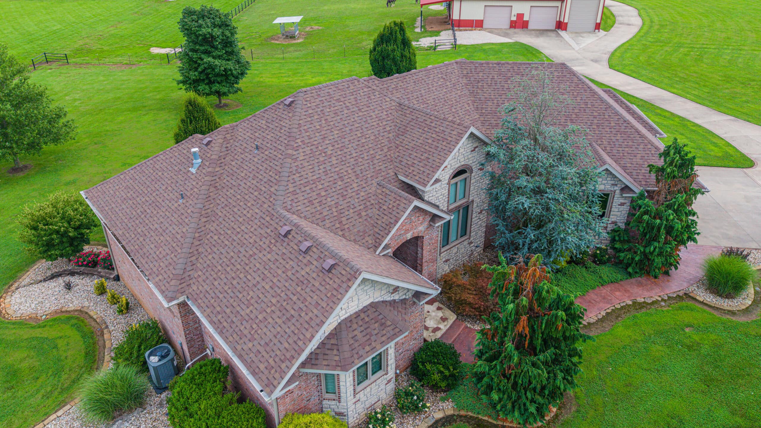 Residential home with new asphalt shingle roof and lush landscaping.