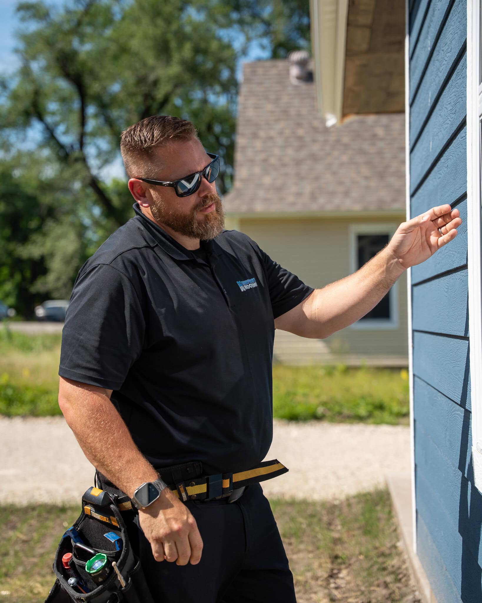 Professional roofing inspector examining blue house siding for damage or maintenance needs.