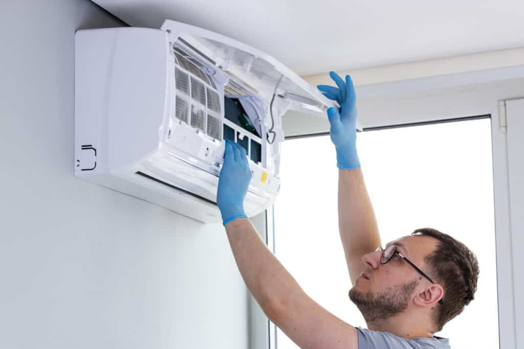 HIGH-QUALITY HVAC TECHNICIAN INSPECTING AND REPAIRING A WALL-MOUNTED AIR CONDITIONER UNIT FOR OPTIMAL COOLING AND HEATING PERFORMANCE. EXPERT HVAC AND PLUMBING SERVICES FROM MY JOCKEY.