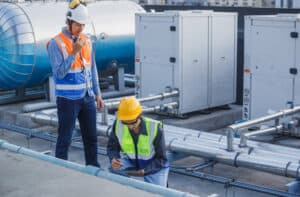 HVAC TECHNICIAN AND ENGINEER INSPECTING INDUSTRIAL HEATING, VENTILATION, AIR CONDITIONING SYSTEMS ON ROOFTOP.