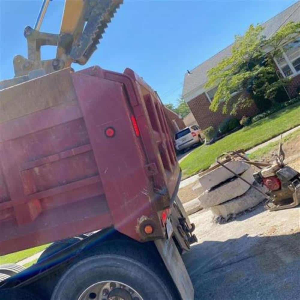 A red dump truck and excavation equipment on a residential street in front of a brick house during a Bison Plumbing sewer line replacement