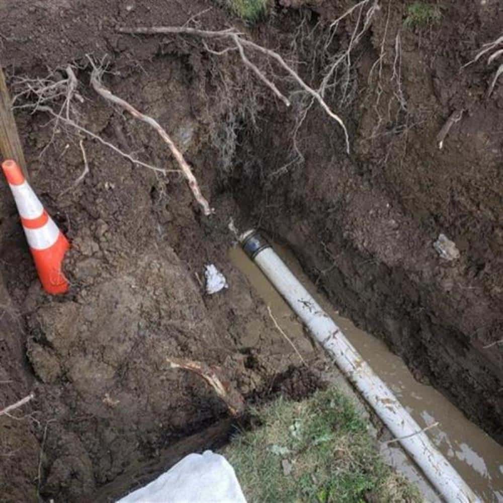 A PVC sump discharge line laid in an exterior trench running away from a Michigan home's foundation on a Bison Plumbing job