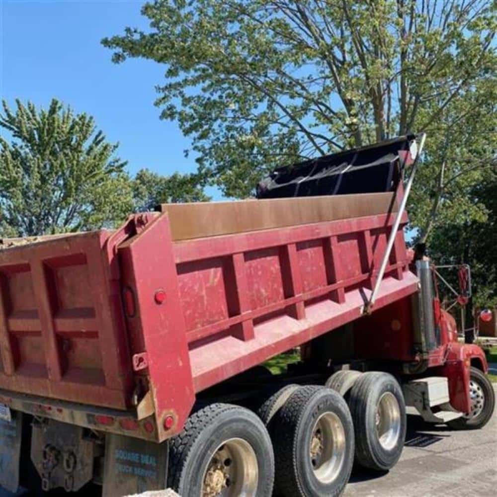 A red dump truck loaded with excavated soil parked on a tree-lined residential street during a Bison Plumbing sewer lateral replacement