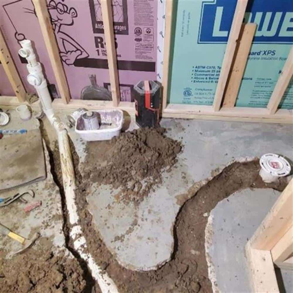 A perimeter drain tile trench cut along a basement foundation wall with the drain line laid before the sump pit tie-in, on a Bison Plumbing installation