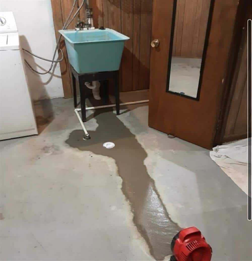 A wet basement floor with water pooling around a laundry tub after a sump pump failure in a Michigan home