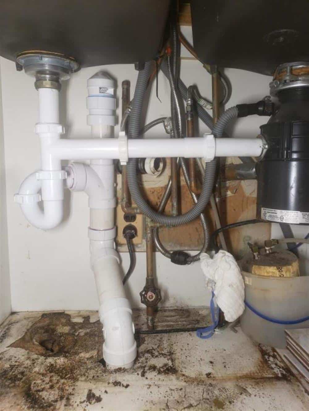 New white PVC drain and vent connections beneath a utility sink, with braided supply lines and a disposal unit in a basement laundry area