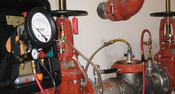 A close-up view of fire sprinkler system equipment—red pipes, valves, gauges, and hoses connected to a pressure testing device. This indoor setup highlights the precision found with plumbers in Warren MI.
