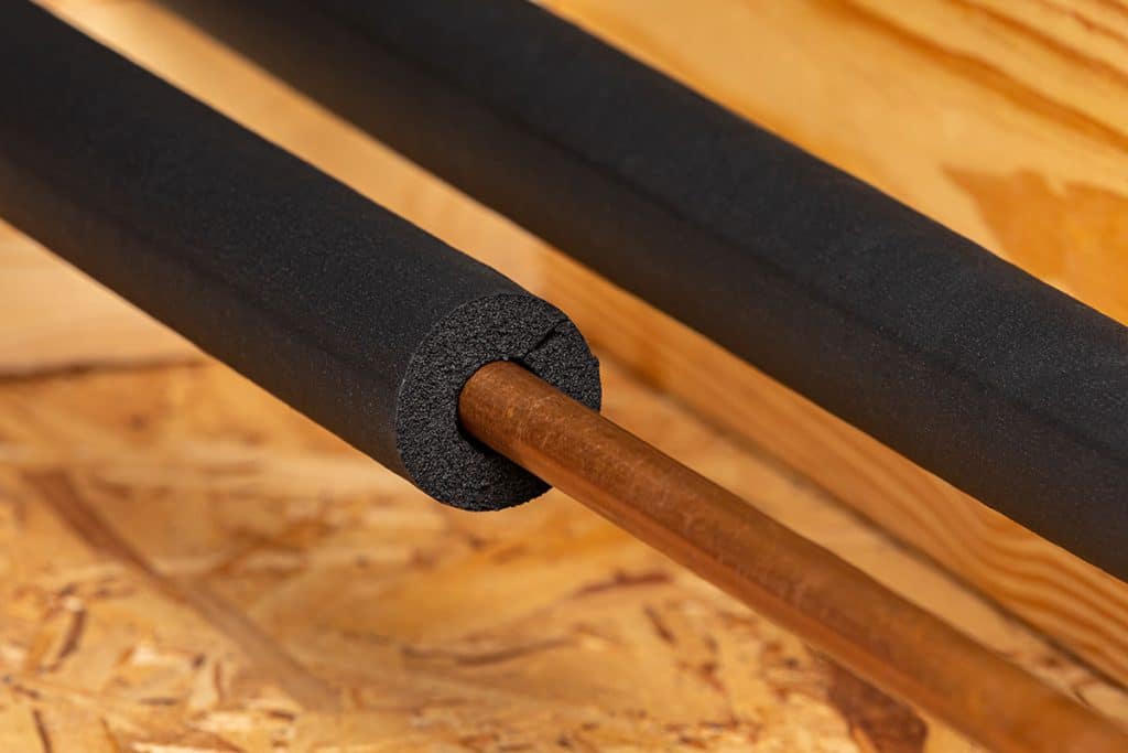 A close-up of a copper pipe partially covered with black foam insulation, resting on a wooden surface with another insulated pipe next to it—perfect for projects handled by a skilled plumber near me.
