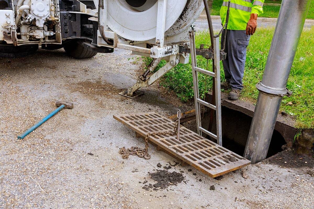 A worker in a reflective jacket stands beside an open storm drain, next to a bison plumbing warren michigan maintenance truck. Tools and equipment are set up for cleaning or No-Dig Sewer Repairs.