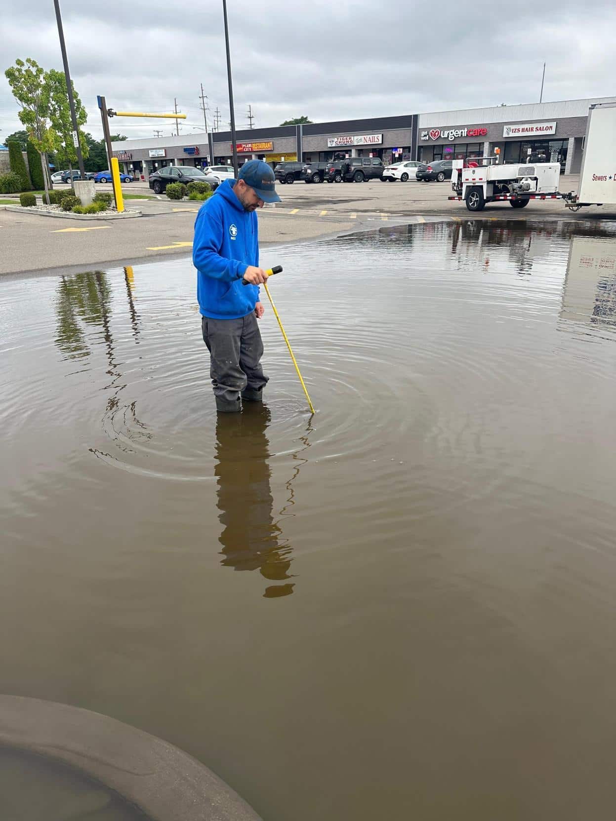 A Bison Plumbing technician standing in floodwater with a measuring gauge after a heavy rain event in Southeast Michigan