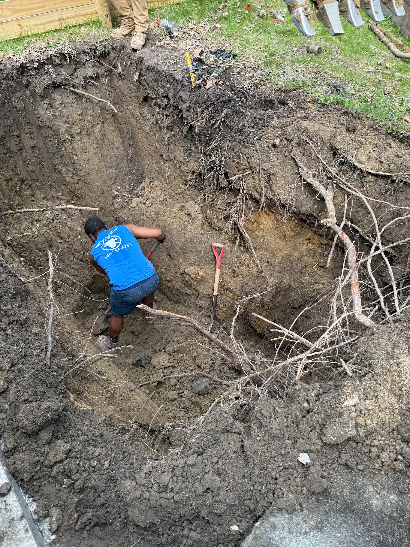 Bison Plumbing technician working in an open sewer excavation with severed tree roots visible through the trench wall