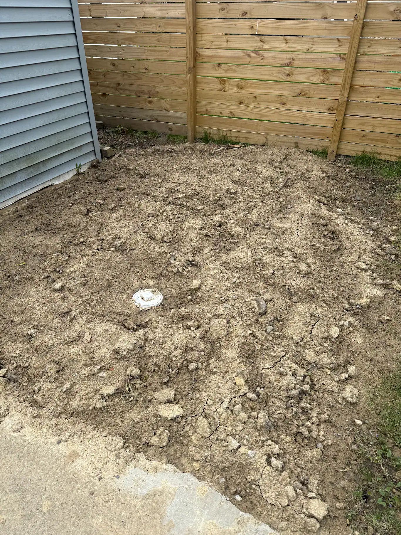 Backfilled and graded ground alongside a Metro Detroit home after an open-cut sewer excavation, at the surface restoration stage