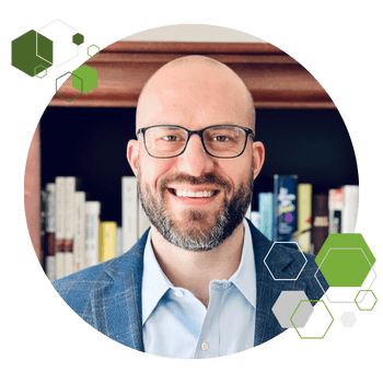 Professional man with glasses smiling, in front of bookshelves.
