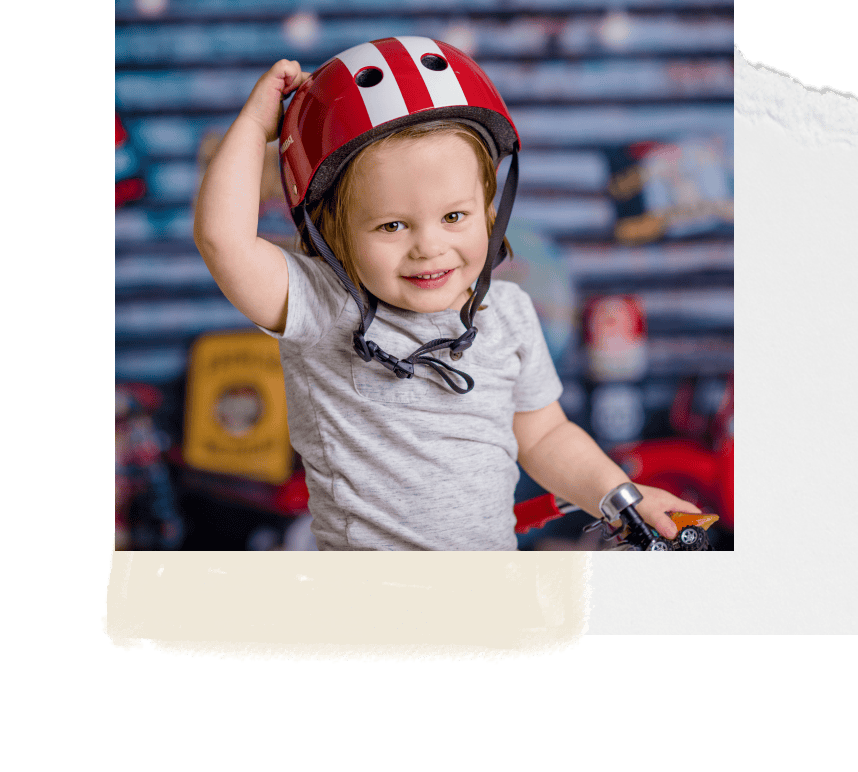 Cute young child wearing a red bike helmet, smiling with spotty background, capturing joyful childhood moments.