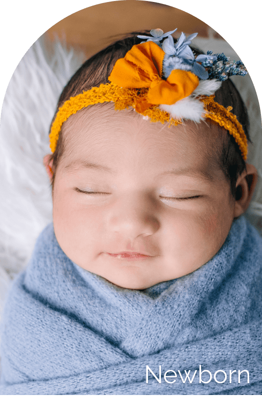 Baby girl sleeping peacefully with floral headband and cozy blue blanket, newborn photography session capturing innocence and tenderness.
