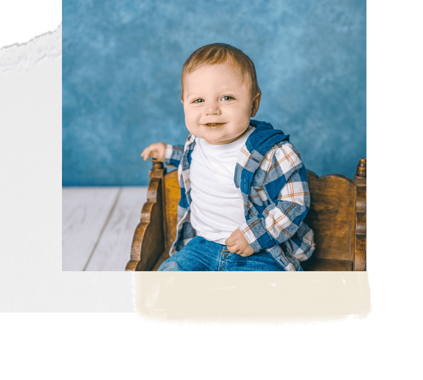 Adorable young child sitting on vintage wooden chair, smiling and looking at the camera, indoor family photography, natural light, colorful casual clothing.