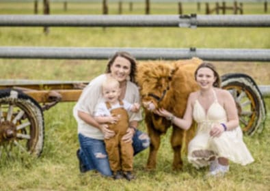 A joyful family portrait outdoors with a lion sculpture, featuring a mother, two children, and a lion, capturing candid moments and cheerful expressions in a natural setting.