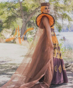 Robe longue, haut drapé, en tissu batik couleur moutarde et marron. Avec ceinture large brodée et tulles traîne brillant marron. Foulard et chapeau brodé assortis.