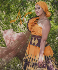 Robe longue, haut drapé, en tissu batik couleur moutarde et marron. Avec ceinture large brodée et tulles traîne brillant marron. Foulard et chapeau brodé assortis.