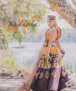 Robe longue, haut drapé, en tissu batik couleur moutarde et marron. Avec ceinture large brodée et tulles traîne brillant marron. Foulard et chapeau brodé assortis.