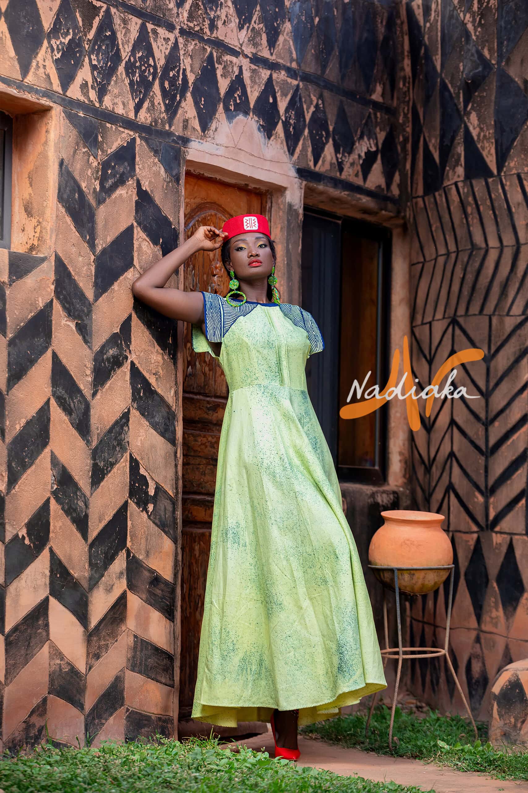 Robe longue de couleur verte, brodée en teinture à jets , ovale de la taille jusqu'au bas assortie d'un chapeau Apéto rouge à motif blanc