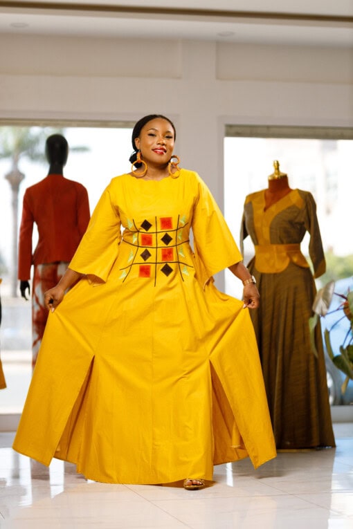 Longue robe brodé de couleur jaune moutarde avec manches 3/4 en tissu coton woodin avec des broderies à l'avant. La robe est agrémentée de fentes en bas sur chaque coté de la robe
