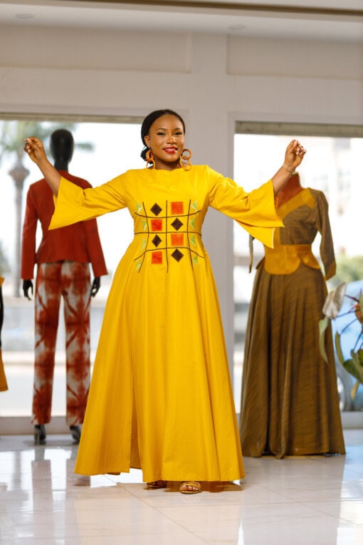 Longue robe brodé de couleur jaune moutarde avec manches 3/4 en tissu coton woodin avec des broderies à l'avant. La robe est agrémentée de fentes en bas sur chaque coté de la robe