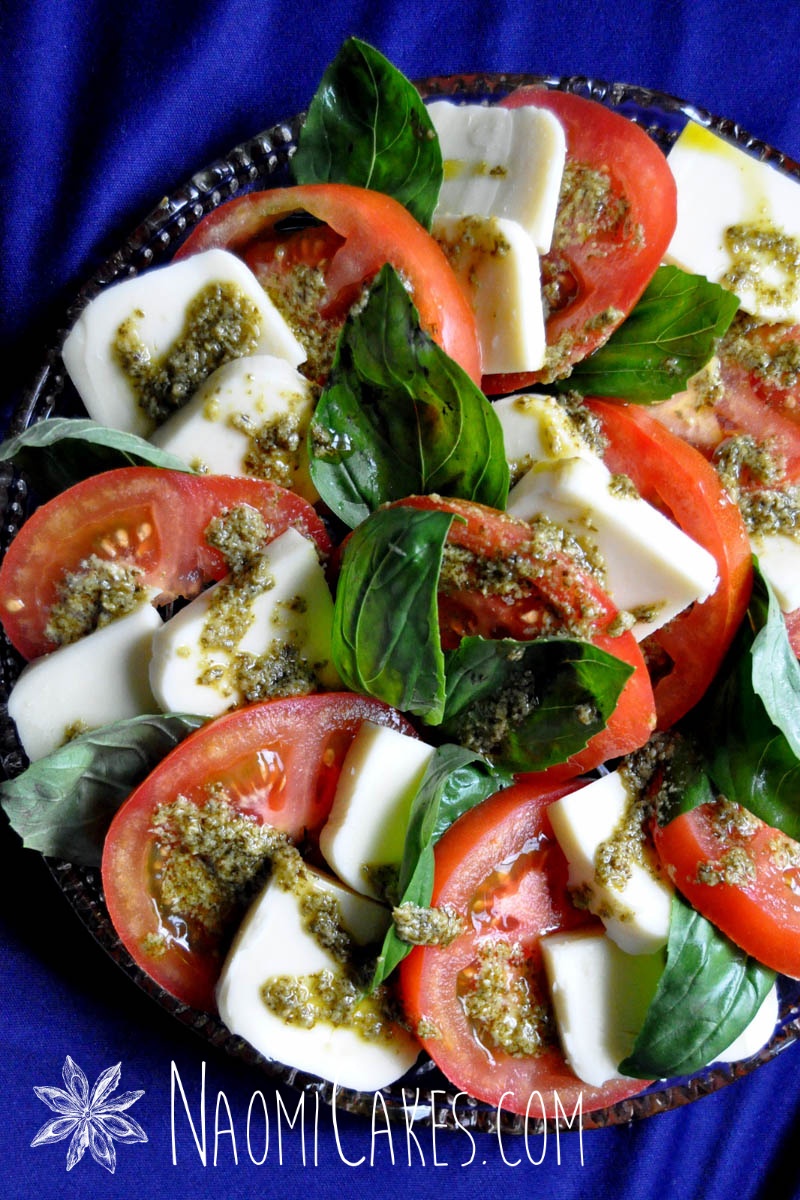 tomatoes, pesto, fresh basil, and mozzerella on a round clear platter with a blue tablecloth in the background